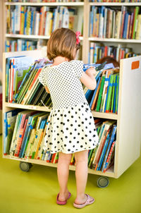 Rear view of girl selecting book while standing in library