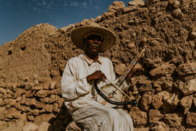 Full length of man holding umbrella against stone wall