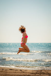 Side view of young woman jumping on shore at beach