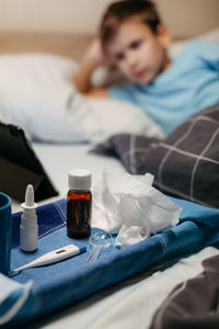 Bottle with antipyretic syrup, nasal spray and thermometer on napkin. little boy on background 