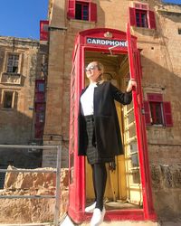 Low angle view of mid adult woman wearing sunglasses standing at telephone booth