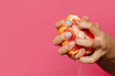 Close-up of hand holding apple against pink background
