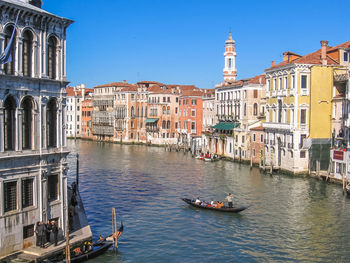 Boats in canal amidst residential buildings against clear blue sky