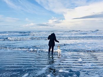 Woman with dog wading in frozen sea against sky