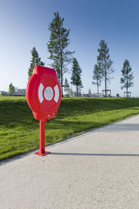 Red road sign on field by street against sky