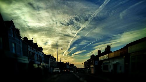 Road amidst buildings against sky during sunset