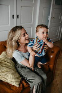 Mother carrying son while sitting on sofa at home