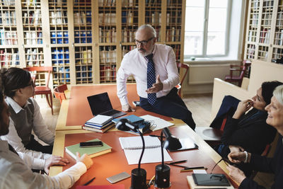 Confident male professional discussing with coworkers sitting at table in law library