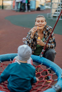 Boy with down syndrome in funny hat walks in the playground with his mother, spinning on a carousel