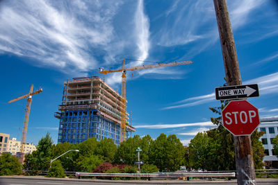 Road sign by trees against sky in city