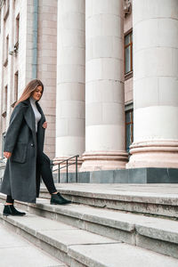 Young brunette woman walking up on stairs. long beautiful hair and long coat in business downtown. 