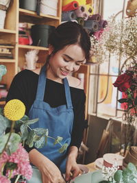 Young woman holding flower while standing by potted plant