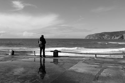 Rear view of man standing on footpath by sea against sky