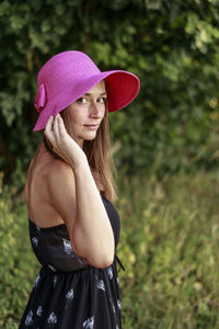 Side view portrait of woman wearing pink hat standing on field