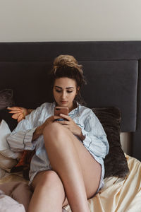 Young woman using mobile phone while sitting on bed at home