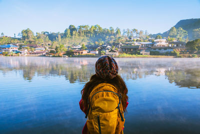 Rear view of woman standing by lake against sky