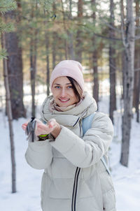 Girl in the winter forest feeds a hungry bird with her hands and looks into the frame smiling