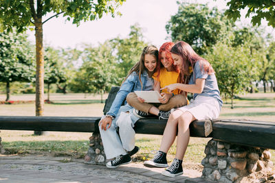 Three charming schoolgirls are sitting on a park bench and preparing for lessons or exams together. 