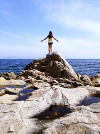 Rear view of woman with arms outstretched standing on rock against sea