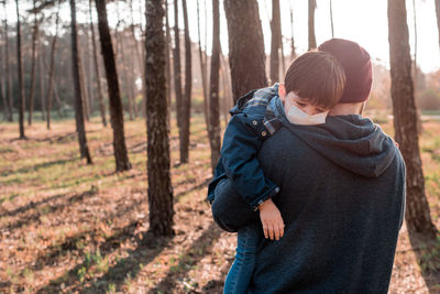 Rear view of man carrying son against trees in forest