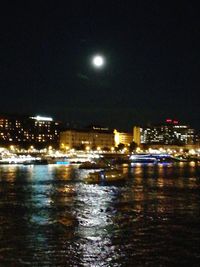 Illuminated city by sea against sky at night