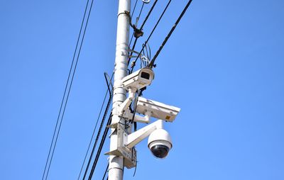 Low angle view of security cameras on pole against clear blue sky