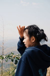Side view of woman shielding eyes against sky