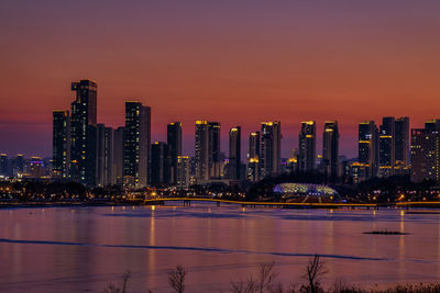 Illuminated city at waterfront during sunset