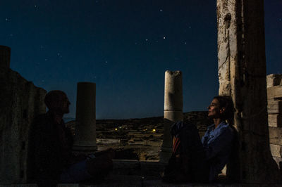 Friends sitting in old ruin against star field at night