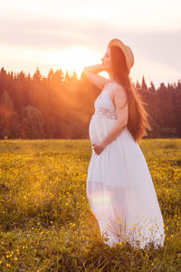 Woman standing on field against sky during sunset