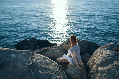 Woman sitting on rock by sea