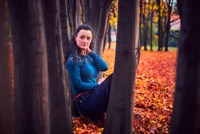 Portrait of smiling young man sitting on tree trunk in forest