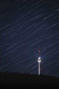 Low angle view of star trails over illuminated communications tower at night