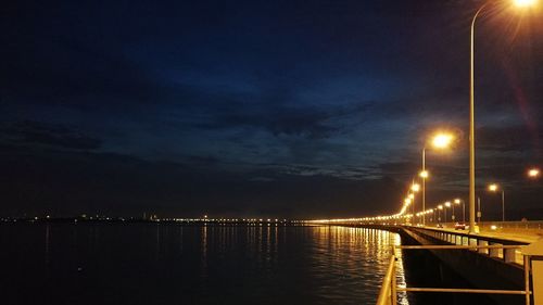 Illuminated bridge over sea against sky at night