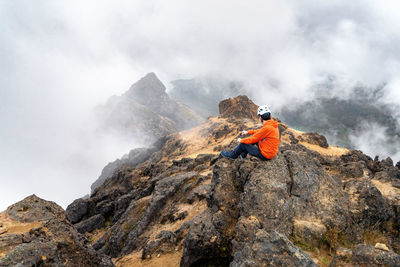 Rear view of man dressed in orange jacket sitting on top of mountain in ecuador