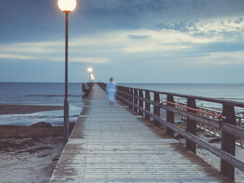 Blurred motion of man walking on pier over sea against sky