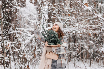 A stylish girl in a snowy forest holds a package from a branch of a nobilis fir and throws snow