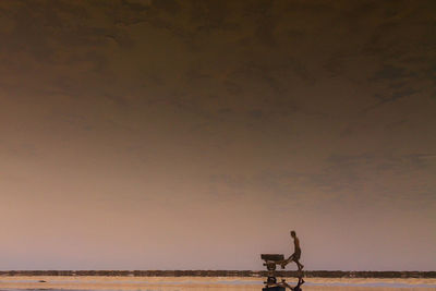 Manual worker pushing wheelbarrow against sky