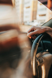 Man's hand is light-skinned with dark hair on the black leather steering wheel of a car