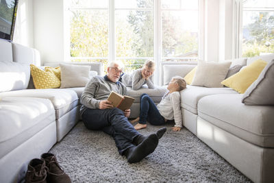 Two girls and grandfather reading book in living room