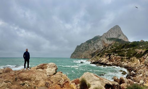 Rear view of man standing on rock against sky