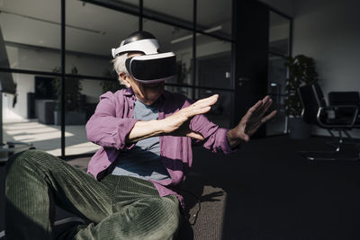Senior businessman gesturing while using virtual reality headset sitting in office