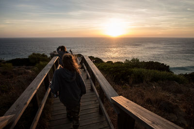 Rear view of woman on sea shore against sky during sunset