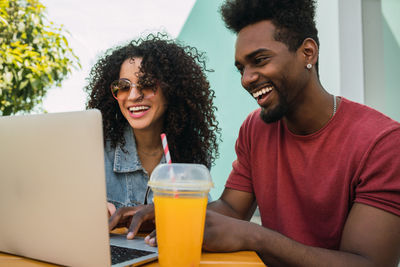 Cheerful friends using laptop outdoors