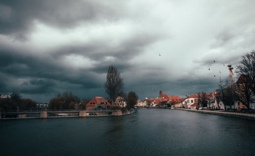 Buildings by river against cloudy sky