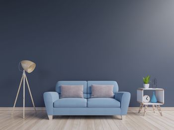 Empty sofa by lamp on hardwood floor against blue wall