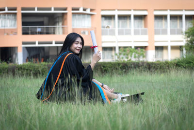 Side view of woman sitting on grass at field