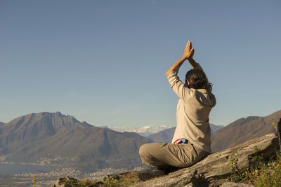 Female hiker with arms raised sitting on cliff against mountains