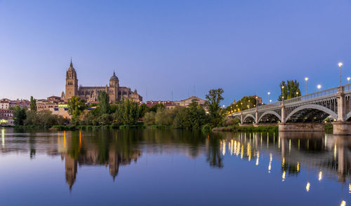 Bridge over river by buildings against clear blue sky