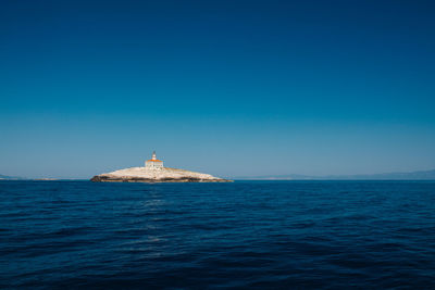 Lighthouse by sea against clear blue sky